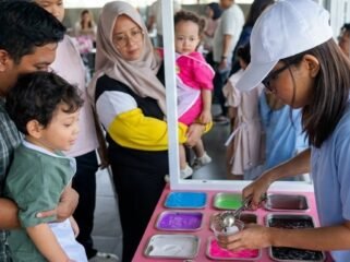 Seorang anak didampingi orang tua mengikuti aktivitas membuat slime berwarna dalam acara slime party interaktif di hotel Surabaya, dengan suasana ramai dan ramah keluarga