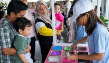 Seorang anak didampingi orang tua mengikuti aktivitas membuat slime berwarna dalam acara slime party interaktif di hotel Surabaya, dengan suasana ramai dan ramah keluarga