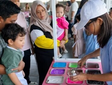 Seorang anak didampingi orang tua mengikuti aktivitas membuat slime berwarna dalam acara slime party interaktif di hotel Surabaya, dengan suasana ramai dan ramah keluarga